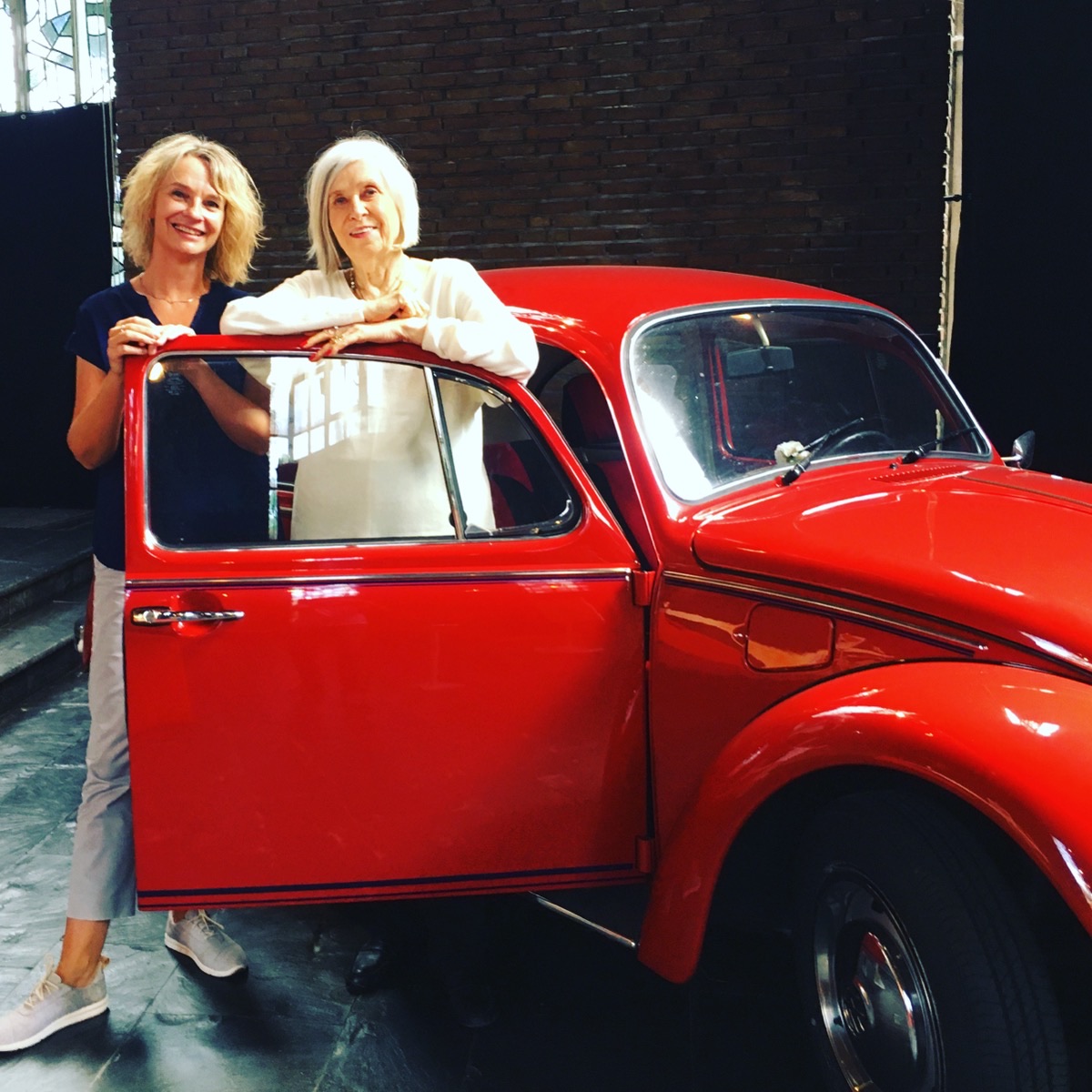Jeanette Nentwig und Gunhild Liljequist lehnen lächelnd an der geöffneten Tür von Jeanettes rotem VW Käfer „Anton“