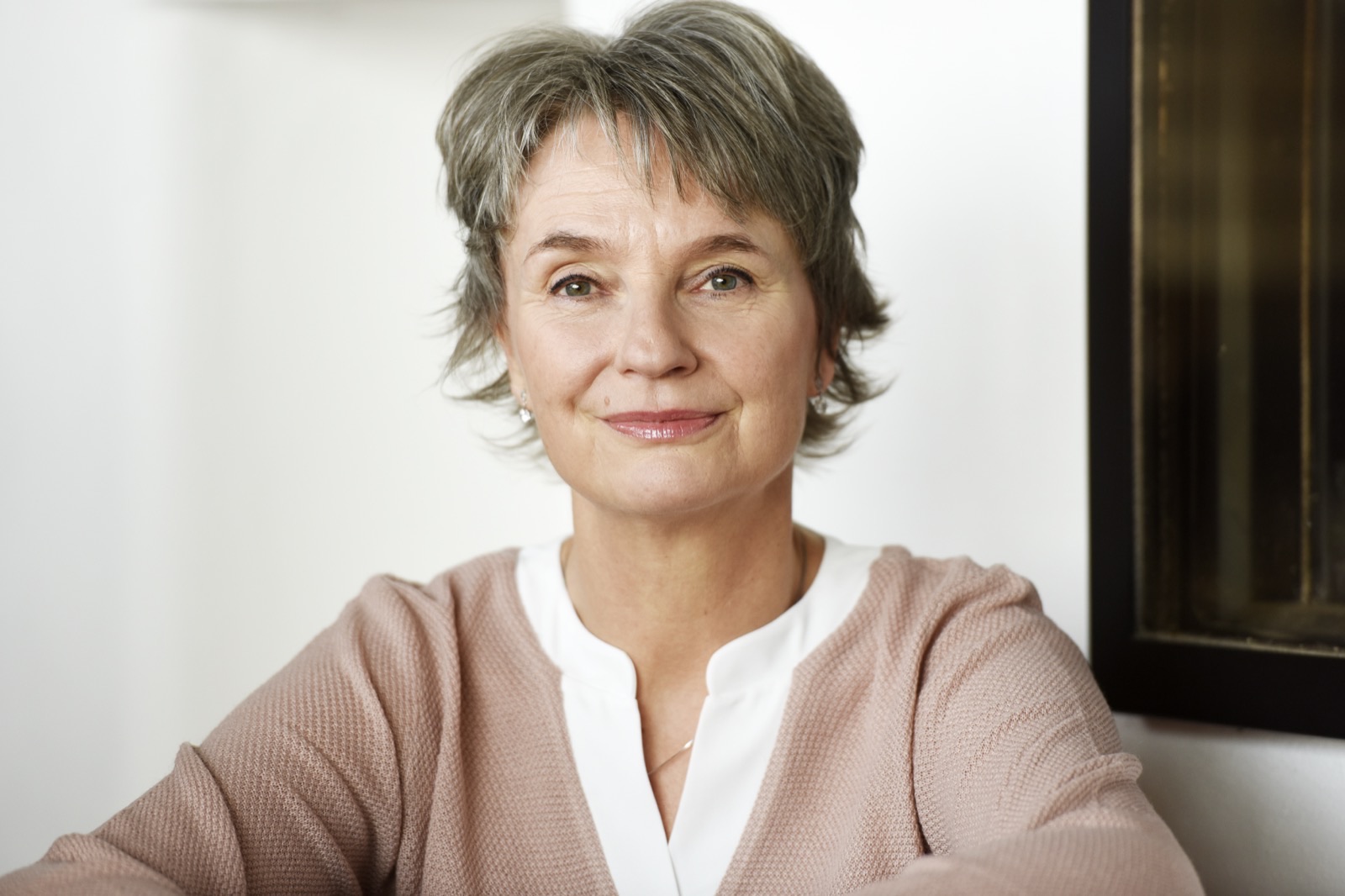 Jeanette Nentwig sitzt in heller Bluse und rosafarbener Strickjacke vor einer weißen Wand und blickt freundlich in die Kamera