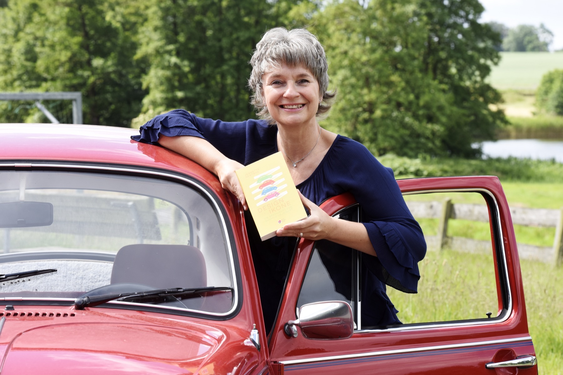 Jeanette Nentwig lehnt an ihrem roten VW Käfer „Anton“ und hält ihr Buch „Design-Ikone“ in der Hand