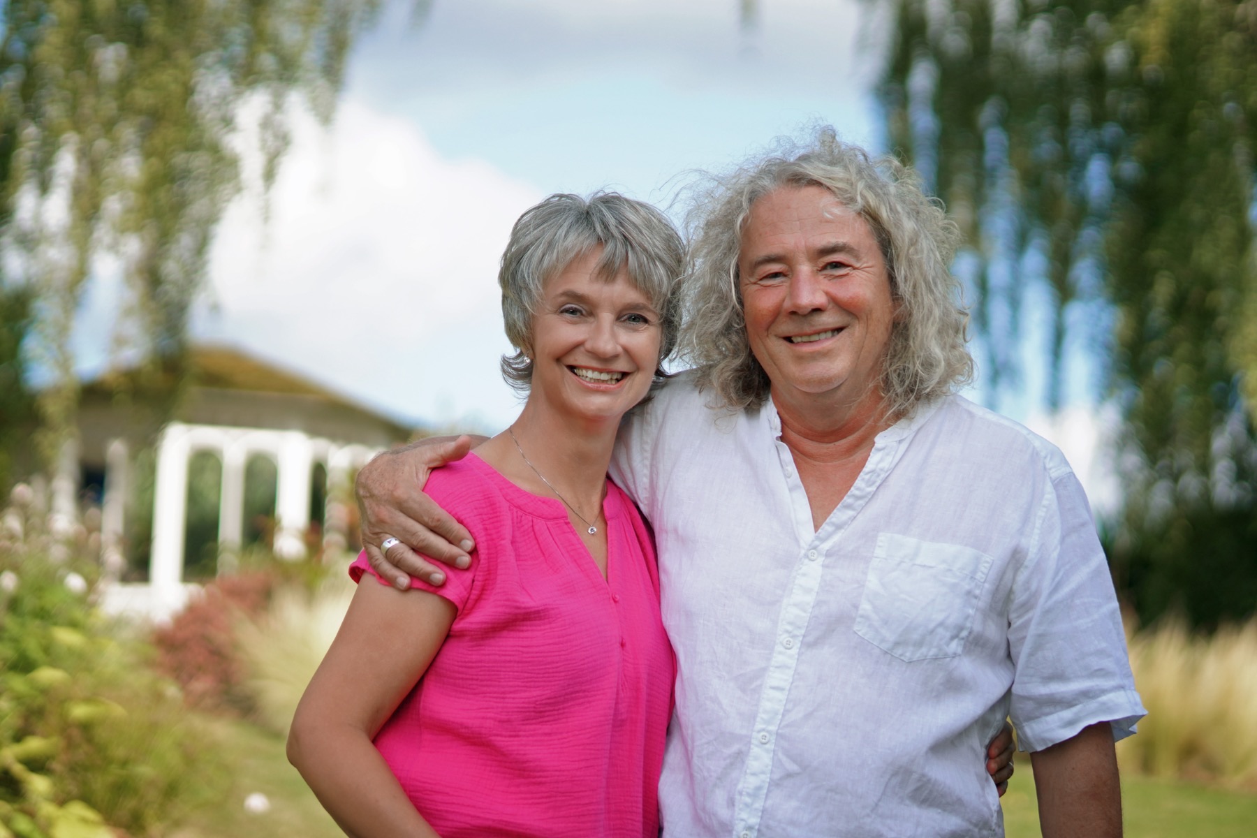 Jeanette Nentwig und ihr Mann Robert Zeidler stehen Arm in Arm in einem Garten und lächeln